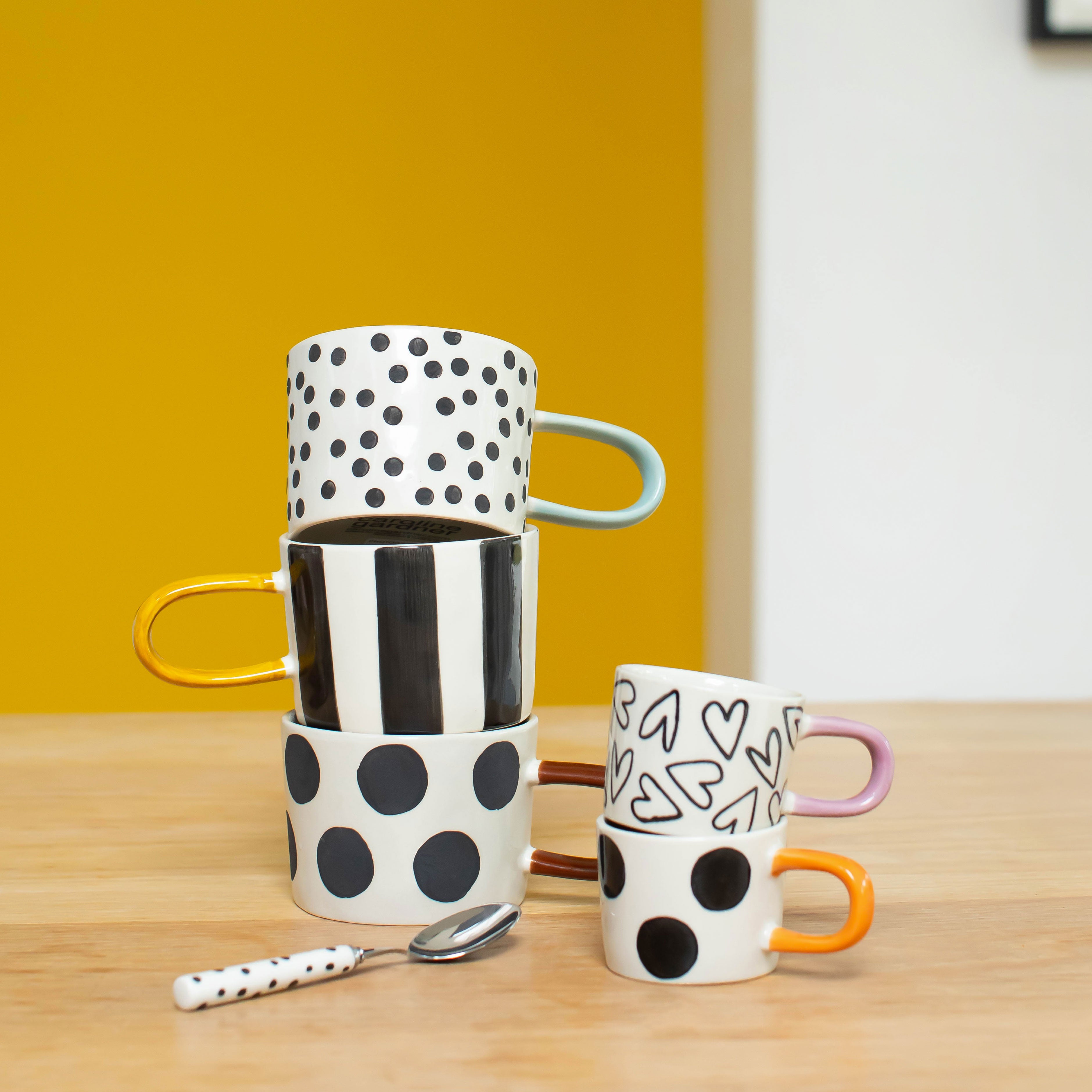 Stack of polka dot and striped mugs on a wooden table with a yellow wall background
