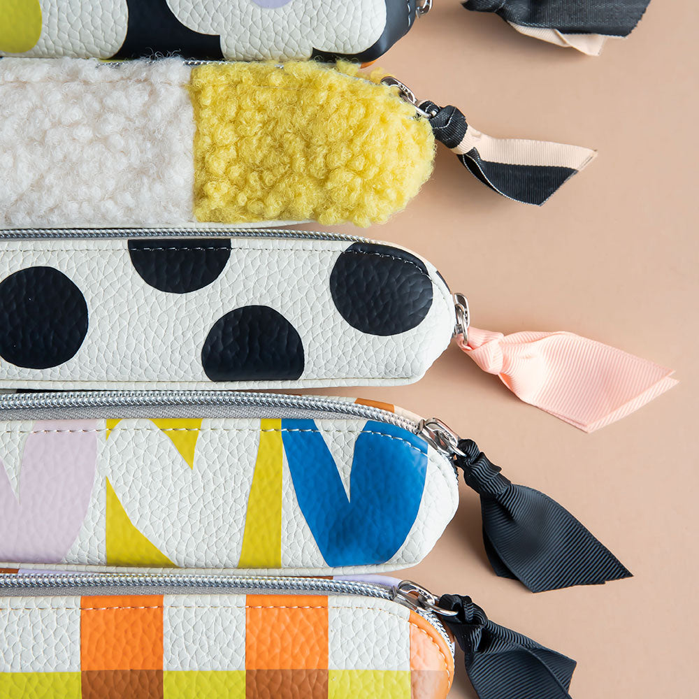 Colourful pencil cases with polka dots and geometric patterns on a beige background