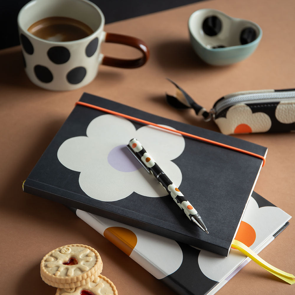 floral print black notebook with a pen, biscuits, and a polka dot cup on a brown surface