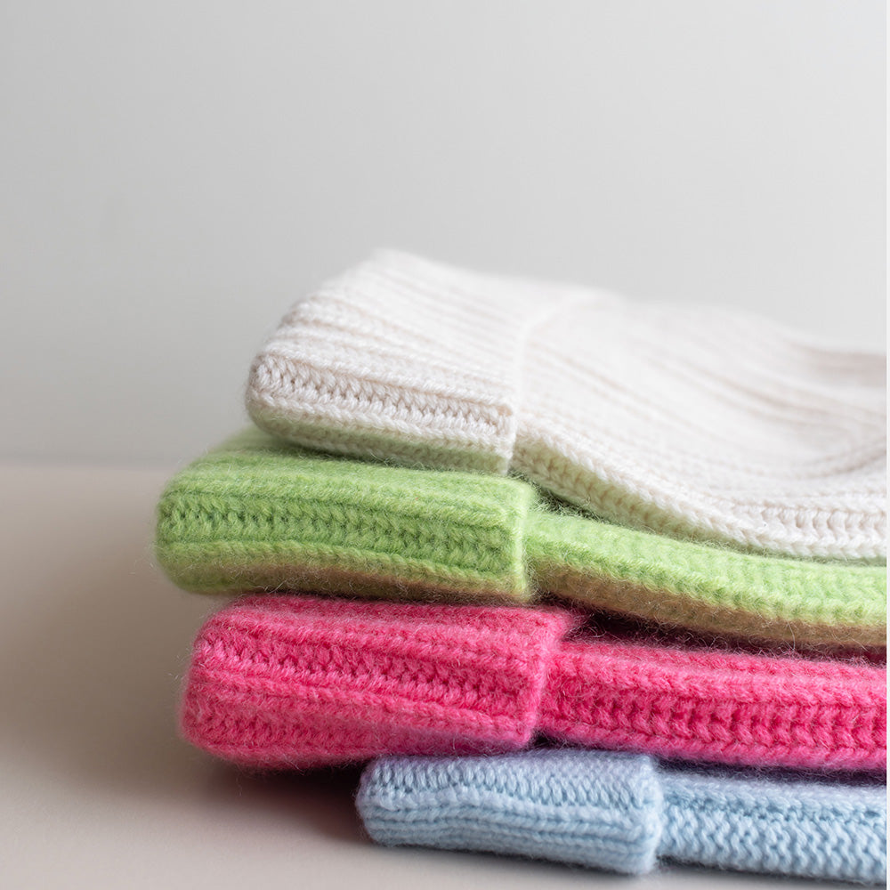 a pile of 4 brushed cashmere beanie hats in cream, green, pink and light blue against an off-white background