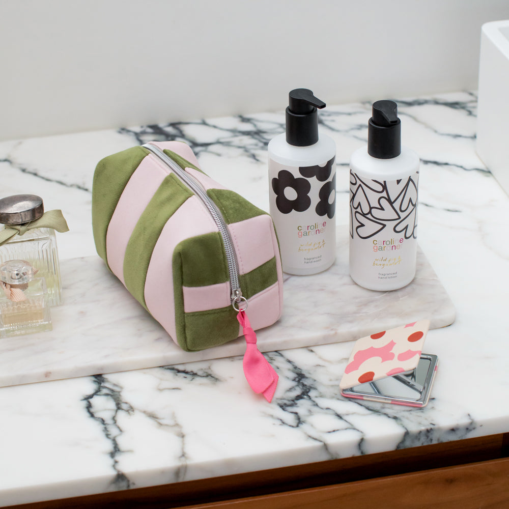 a green and pink striped velvet cosmetic bag on a marble surface with caroline gardner branded toiletries 
