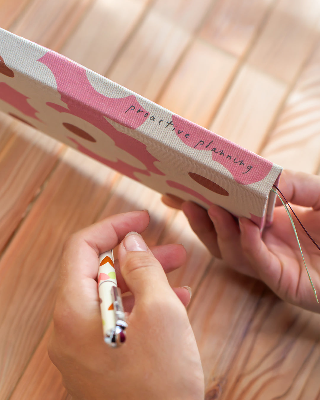A close-up of hands holding a patterned notebook with the words 'practive planning' on the cover, with a pen in the other hand, set against a wooden background.