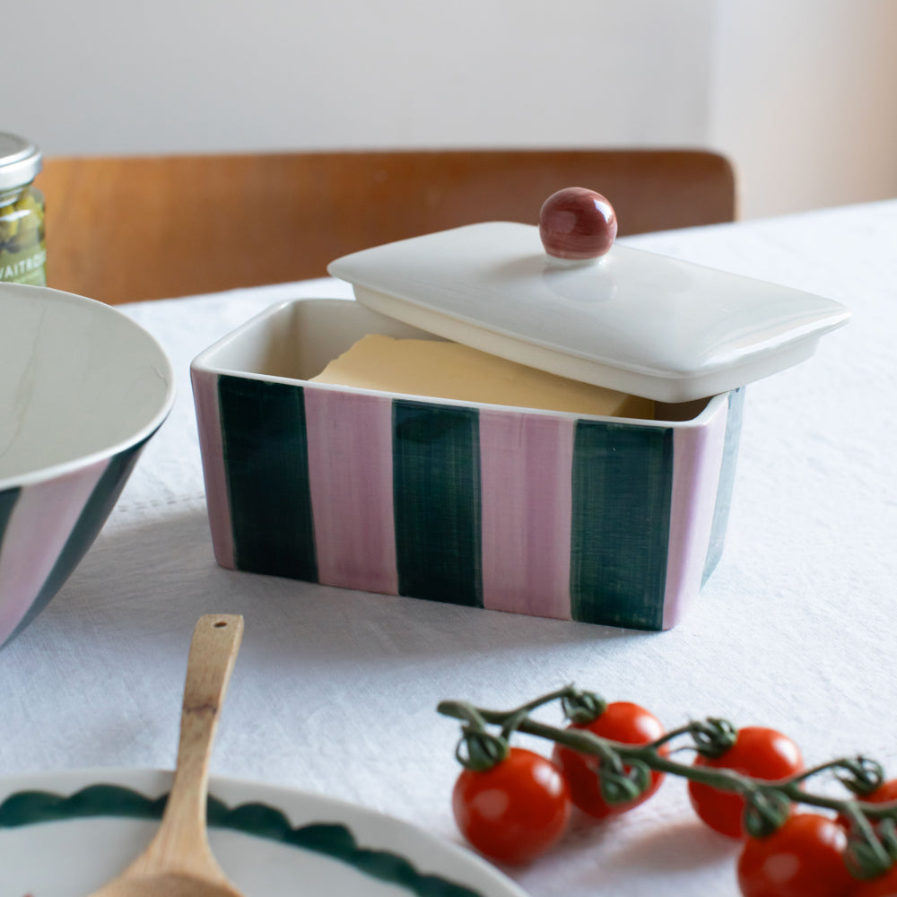 green & pink striped butter dish on a white table clothed table with tomatoes 