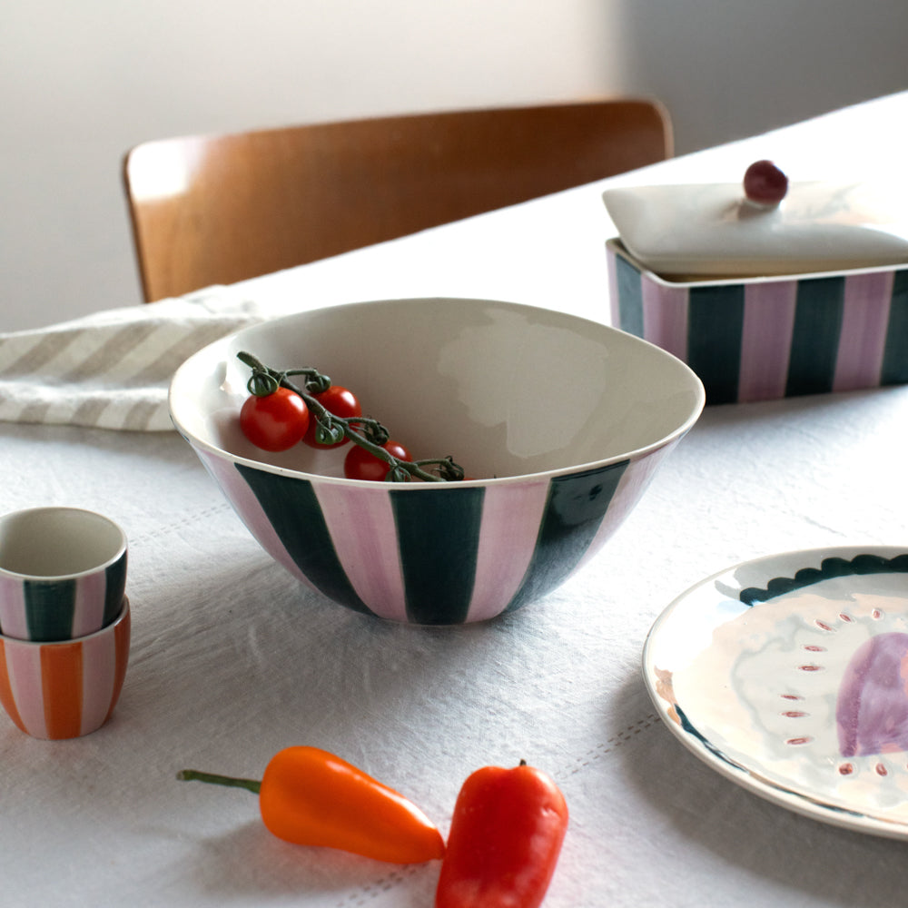 a stylised table scene with a green and pink striped bowl, butter dish and egg cups