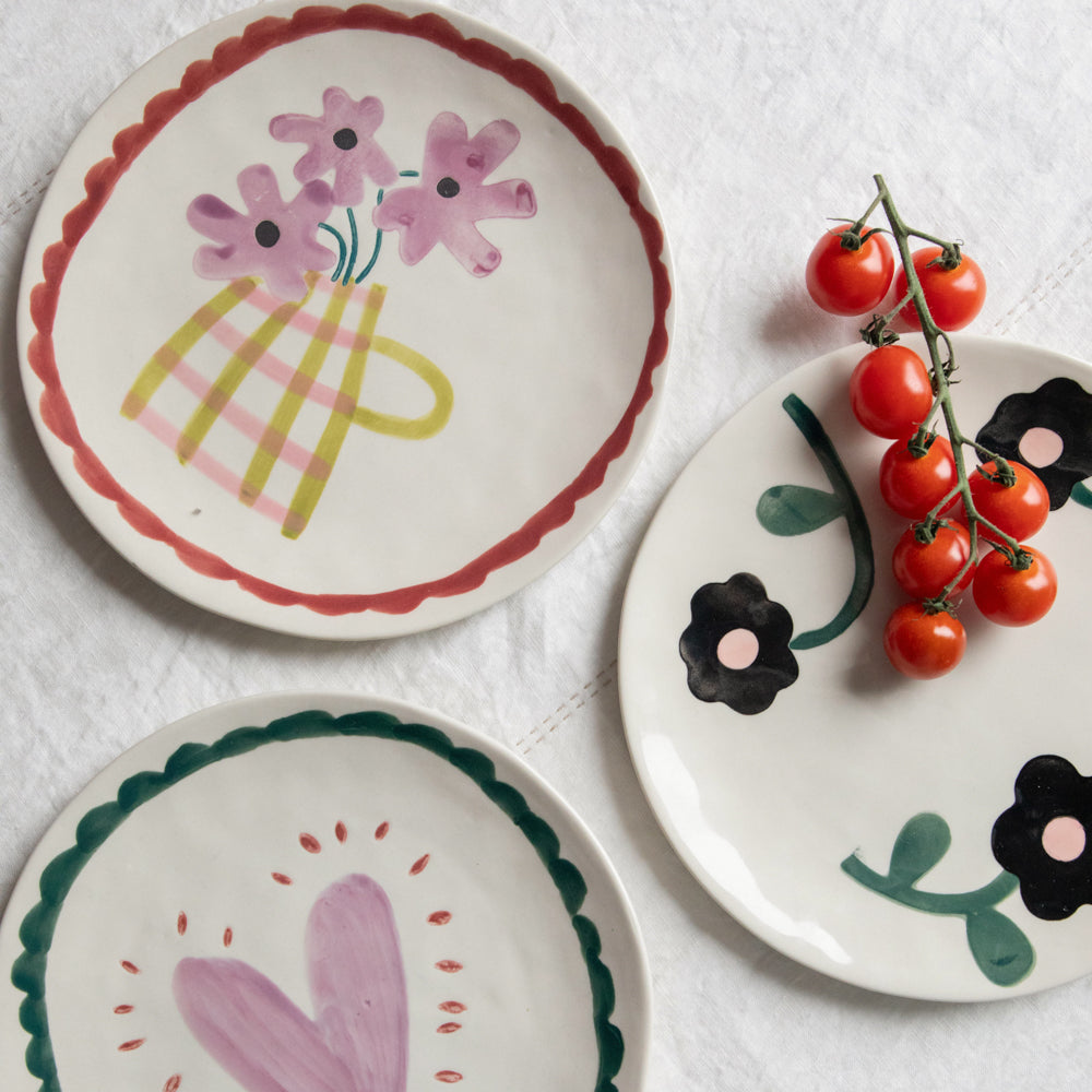 three ceramic plates with floral and heart designs on a white table cloth