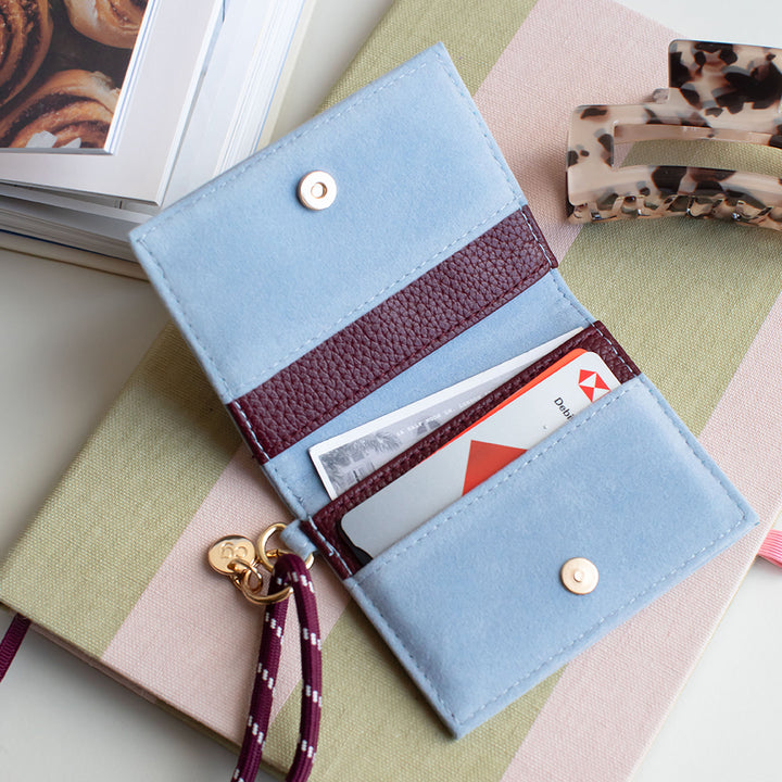 a blue and purple card holder purse on a pink & green striped notebook