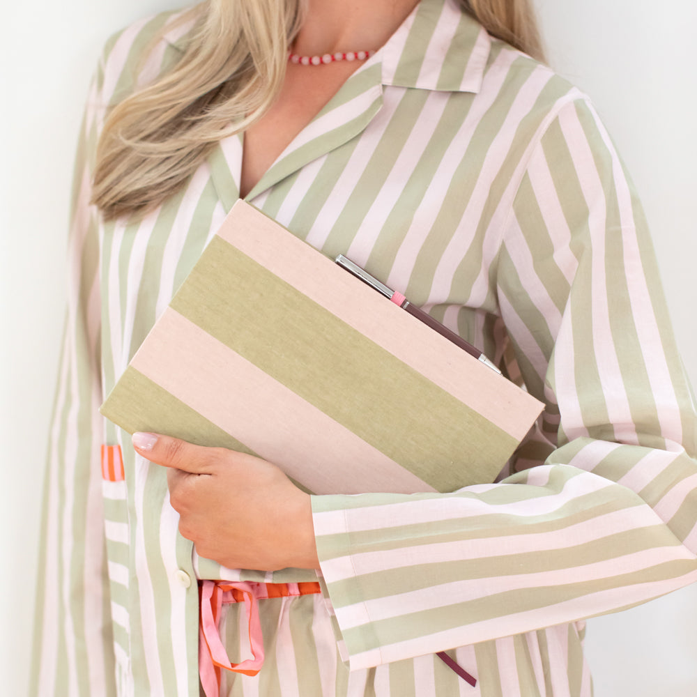 A woman wearing a light green and pink striped long-sleeve shirt holds a matching striped folder or notebook under her arm. The photo is cropped from the neck down against a plain light background.