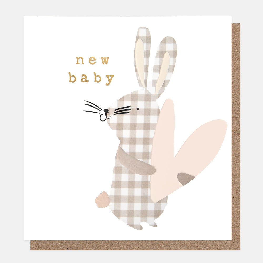 A square greeting card with a kraft envelope, featuring a cute bunny illustration in beige and white gingham with a pale pink wing and the words 'new baby' in gold lettering.