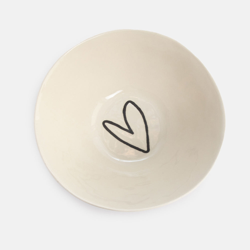 An off-white ceramic bowl with a simple black hand-drawn heart outline in the center, photographed from directly above on a light gray background.