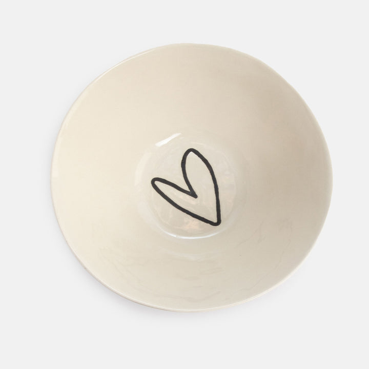 An off-white ceramic bowl with a simple black hand-drawn heart outline in the center, photographed from directly above on a light gray background.