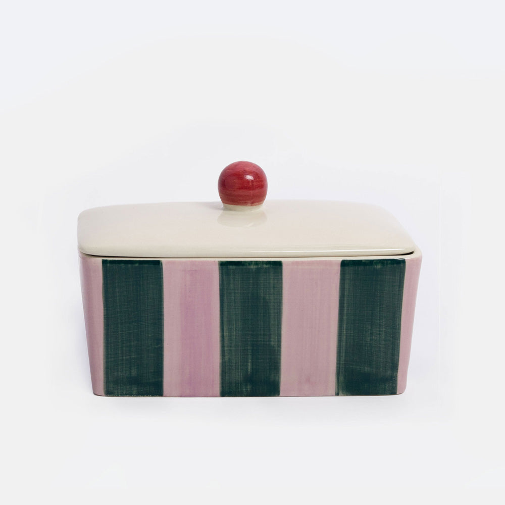 A rectangular lidded ceramic butter dish  with a cream-colored top and lid, featuring vertical stripes in dusty pink and dark green on the sides, topped with a small round red knob, set against a plain white background.