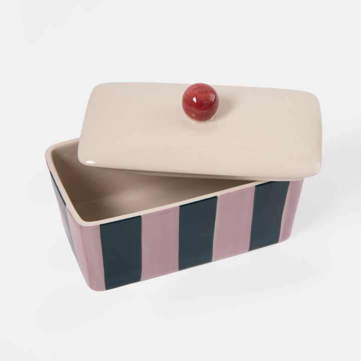 A rectangular ceramic butter dish with a matching lid, featuring vertical stripes in dusty pink, navy blue, and cream, with a small round red knob on top.