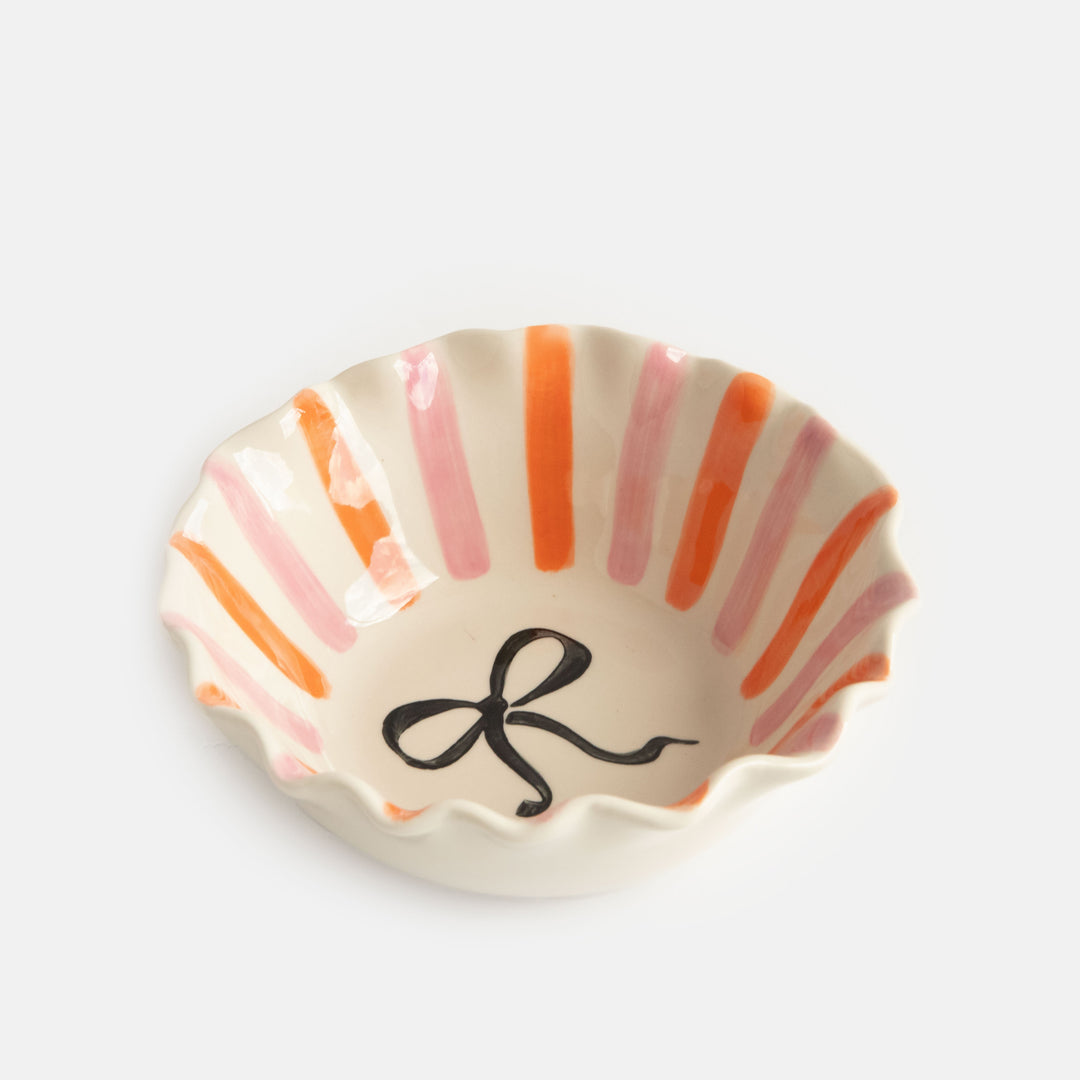 scalloped edge glazed stoneware cereal bowl with pink and orange stripes and black bow design inside
