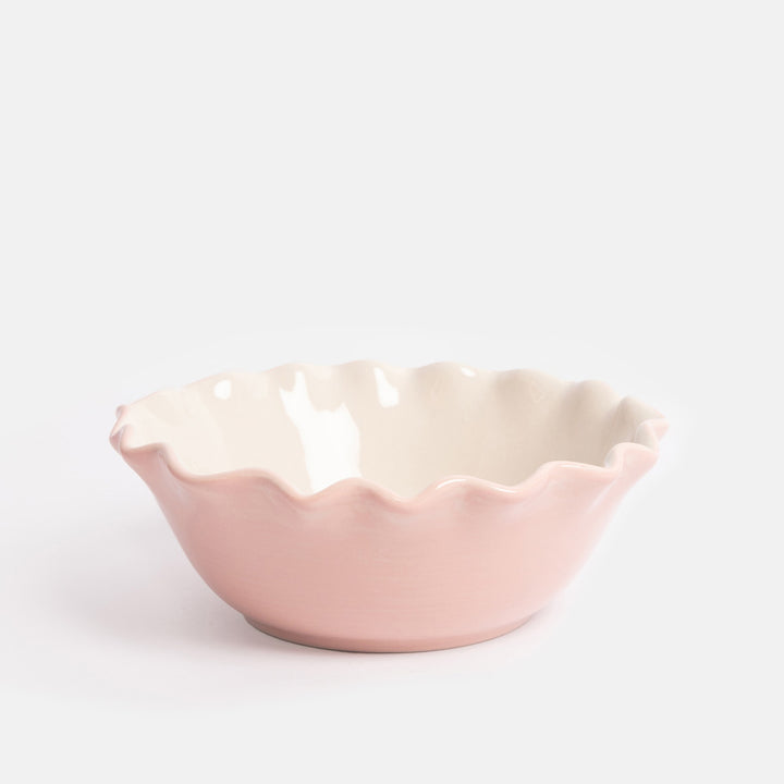 Pink ceramic bowl with scalloped edge on a white background