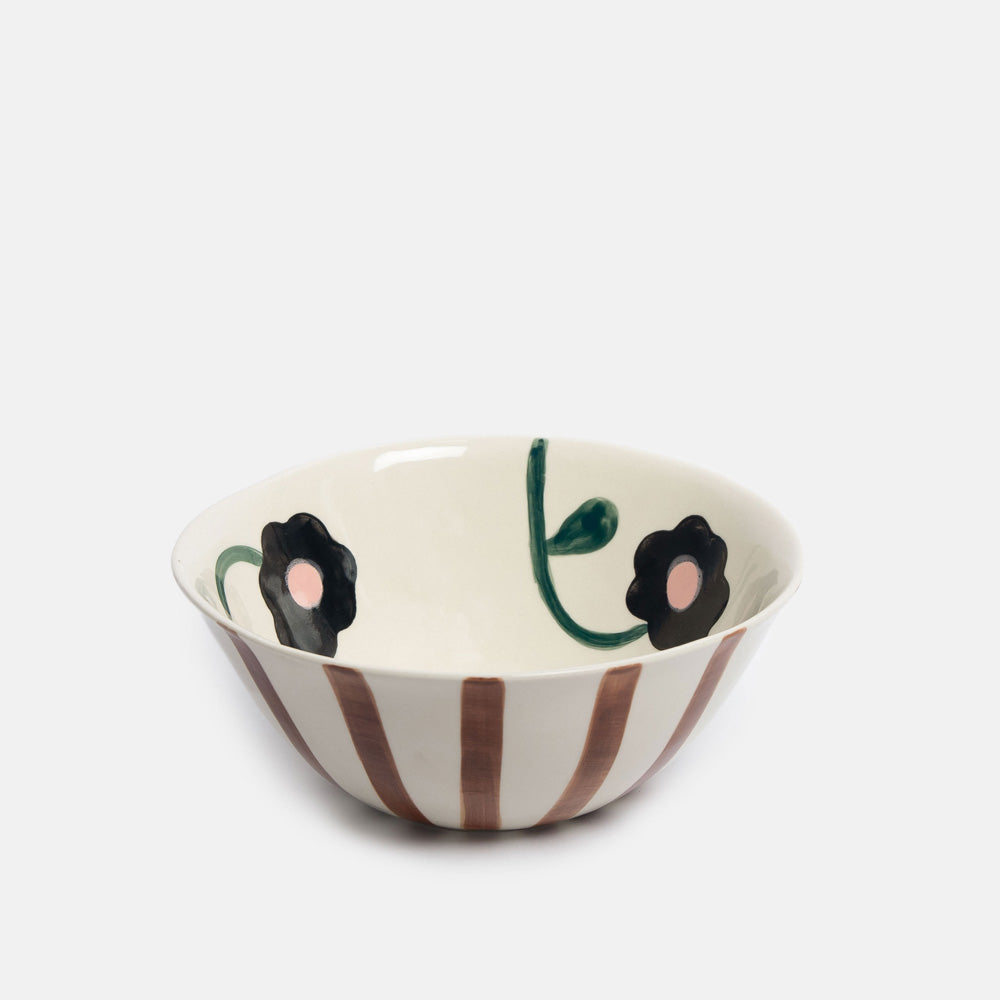 A ceramic bowl with a white base, decorated with brown vertical stripes on the exterior, black flowers with pink centers, and green stems on the interior, shown against a light gray background.