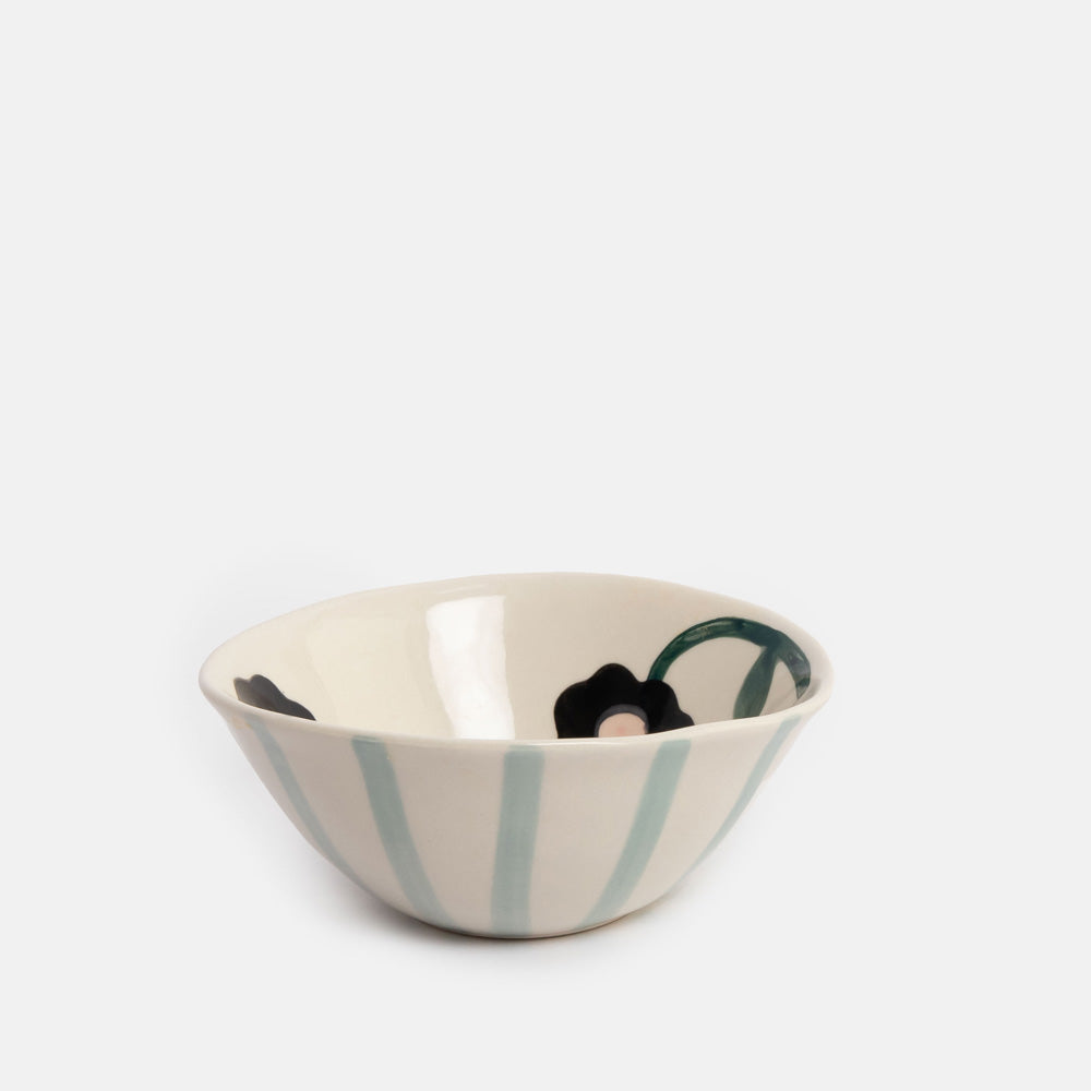 A small ceramic bowl with a cream-colored interior and exterior, featuring vertical light blue stripes on the outside and black floral motifs with a green leaf accent on the inside.