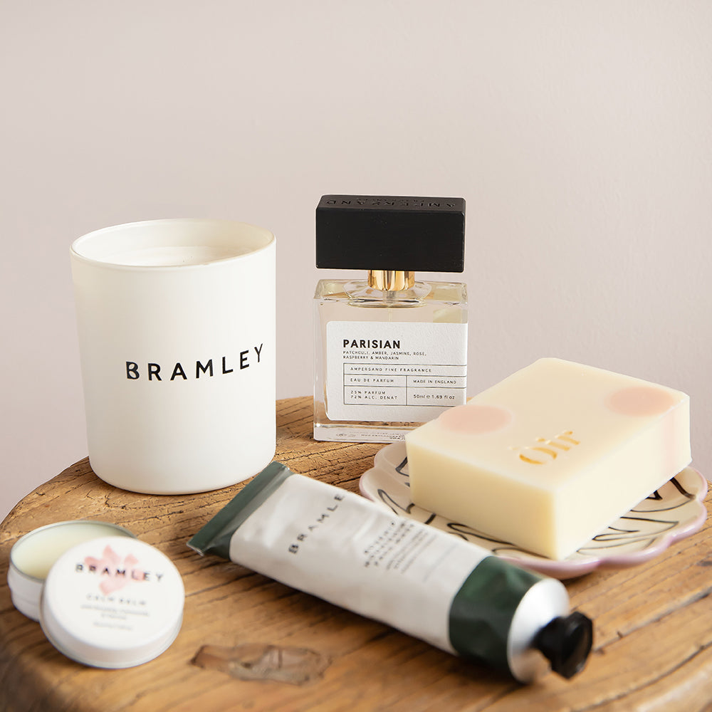 Bramley skincare products including a candle, perfume, soap, and hand cream on a wooden surface.