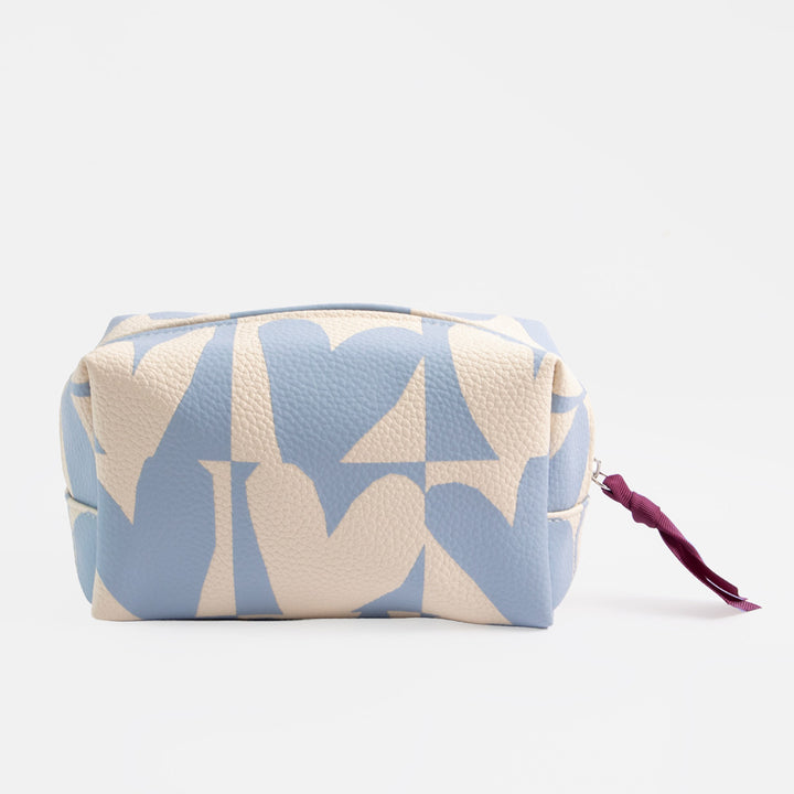 A pebbled faux-leather cosmetic pouch featuring a light blue and cream geometric monogram pattern, with a small dark purple tassel zipper pull on a white background.