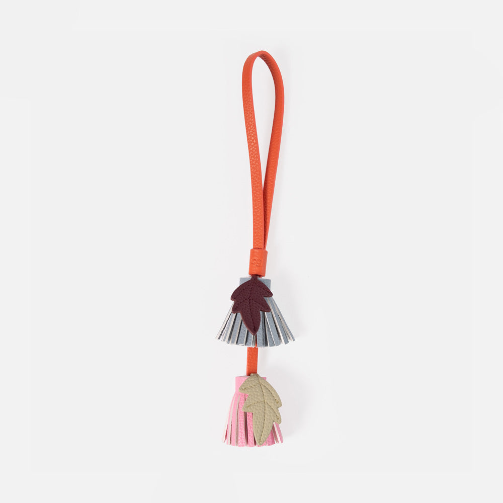 leather look bag charm featuring two tassel flowers on a bright orange strap