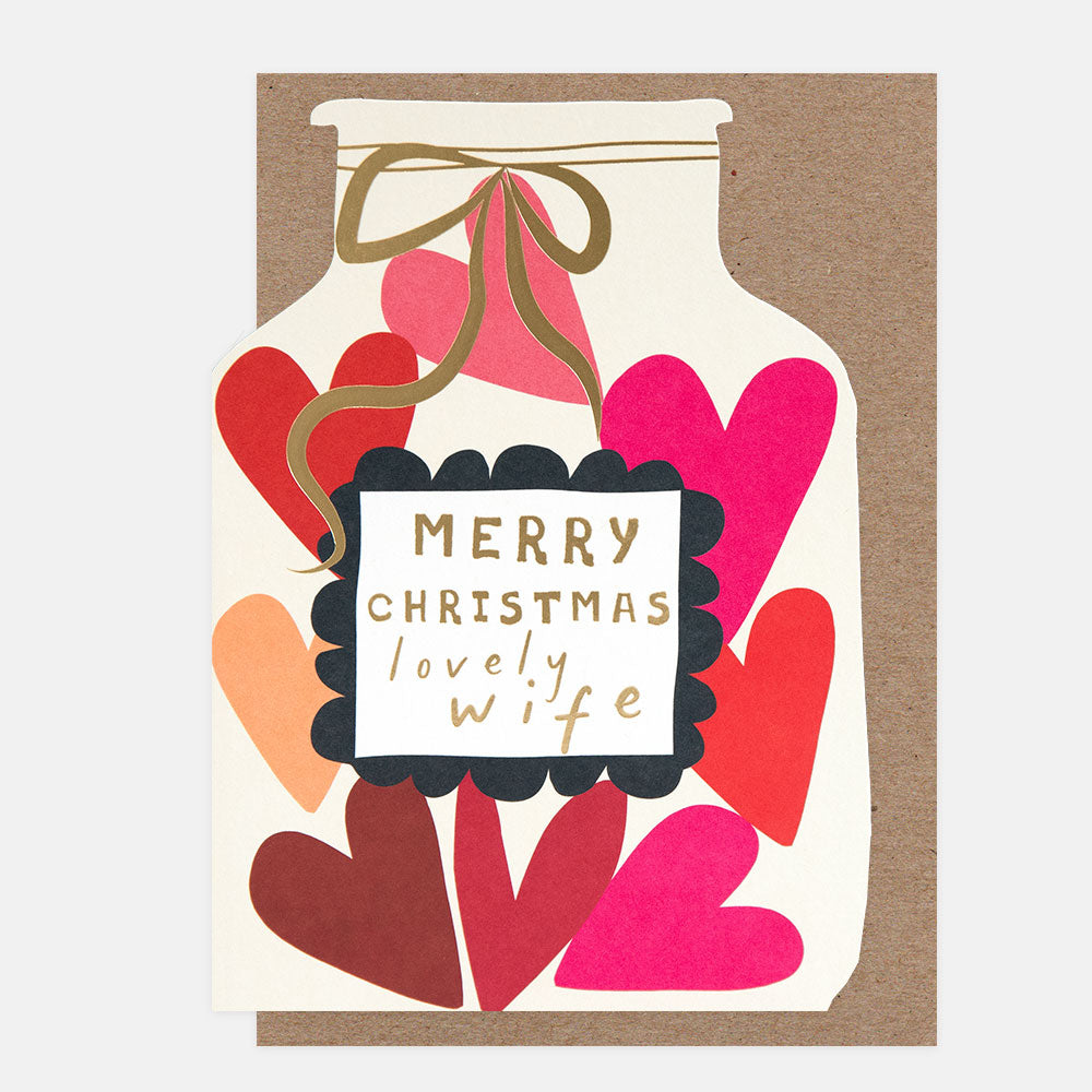 A Christmas greeting card with a bottle-shaped silhouette filled with layered heart shapes in red, pink, orange, and burgundy. A black scalloped label in the center reads “MERRY CHRISTMAS lovely wife” in gold lettering, with a gold ribbon bow at the top.