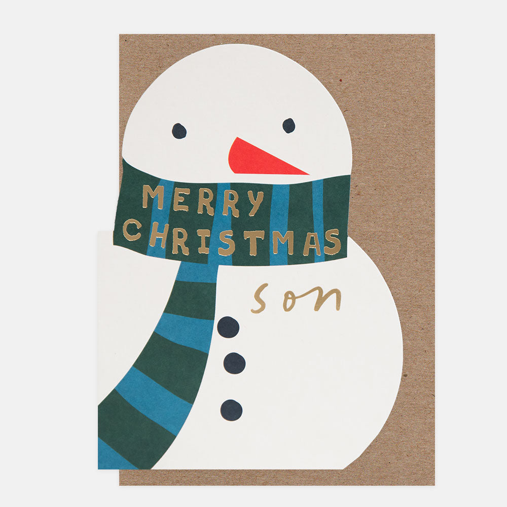 A die cut Christmas greeting card featuring a stylized snowman with a green and blue striped scarf that reads 'MERRY CHRISTMAS' in gold lettering, with 'son' written in gold script below. The card is shown against a plain light background with a brown kraft envelope behind it.