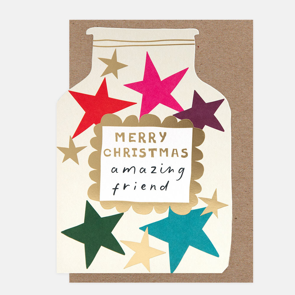 A Christmas greeting card featuring a die cut jar filled with colourful stars in red, pink, purple, green, teal, and gold, with a central label reading 'MERRY CHRISTMAS amazing friend' on a brown kraft envelope against a light grey background.