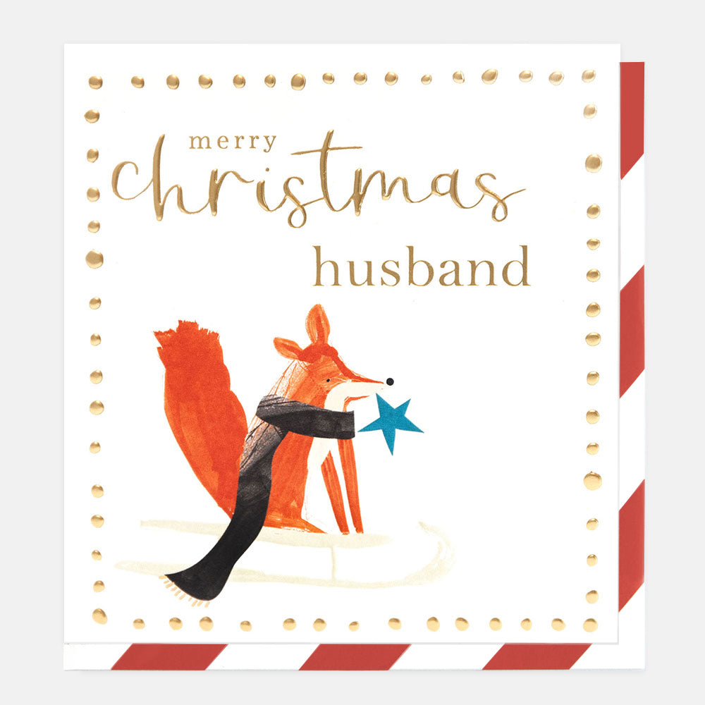 A square Christmas greeting card with the text 'merry christmas husband' in gold script and serif fonts, featuring an orange fox wearing a black scarf and holding a blue star. The card has a white background with gold dotted border details and red-and-white striped edges, shown against a light gray background.
