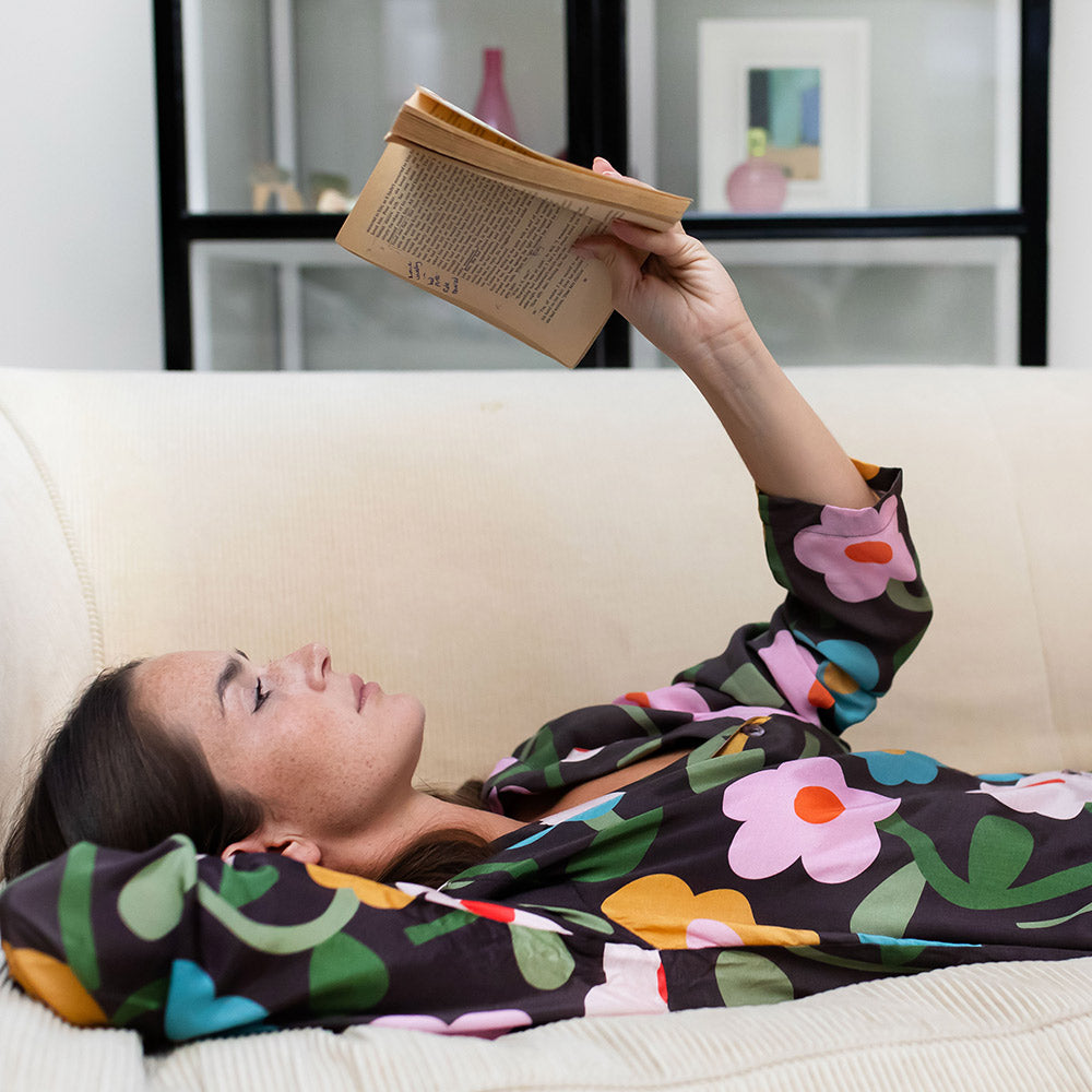 Woman in a floral outfit lying on a couch reading a book