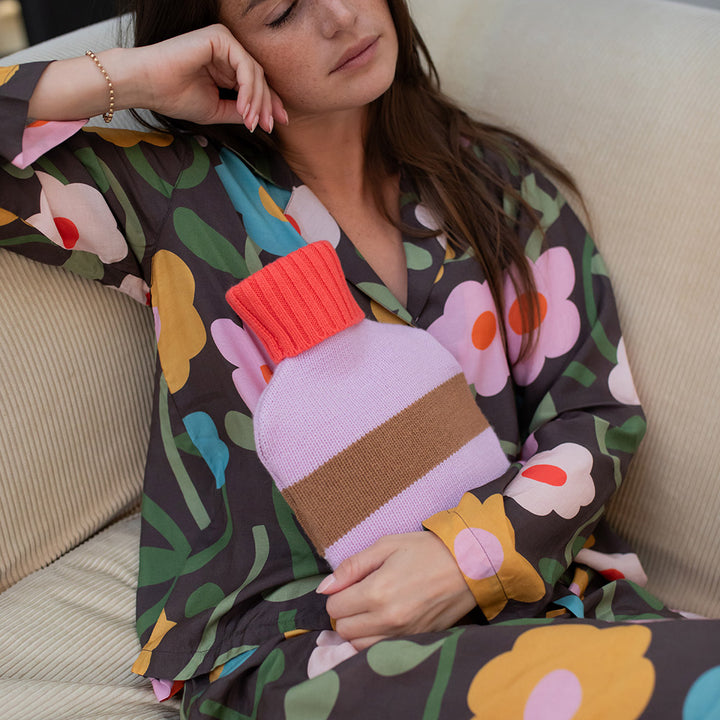 woman in floral pyjamas holding a pink and brown striped hot water bottle