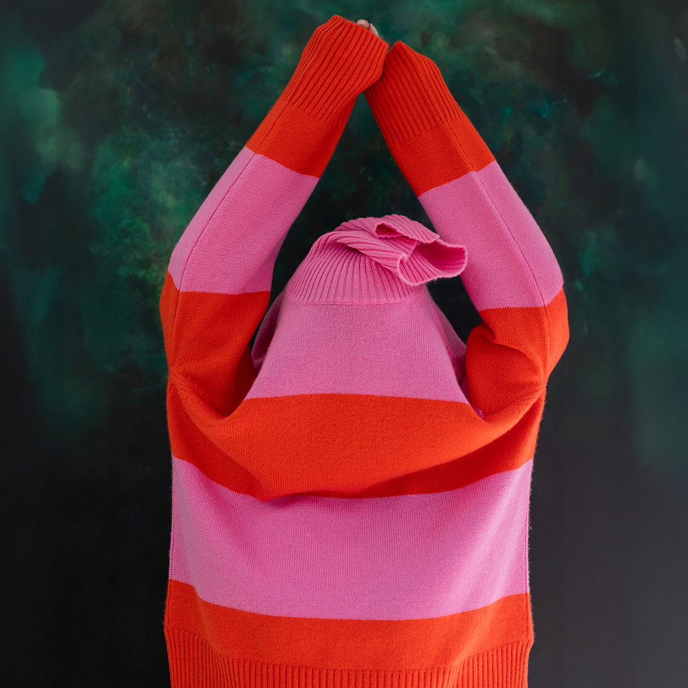 Person wearing a pink and orange striped sweater with arms raised against a dark background