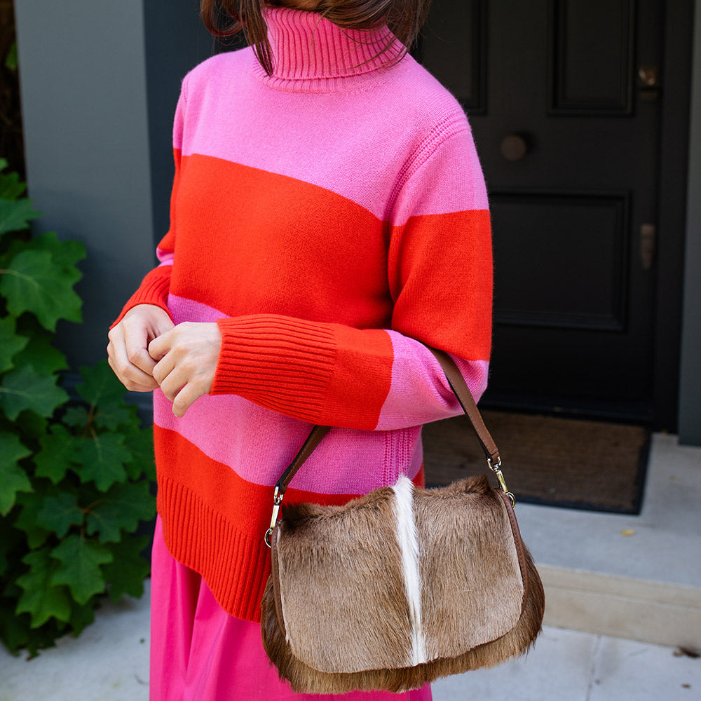 Person wearing a pink and red striped sweater holding a brown fur bag.