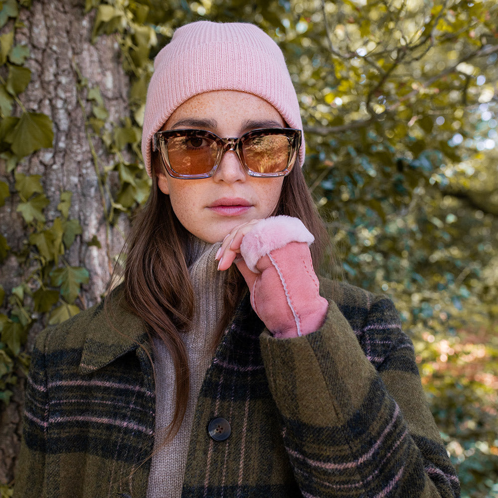 woman wearing a light pink beanie hat, sunglasses and pink suede wrist warmers