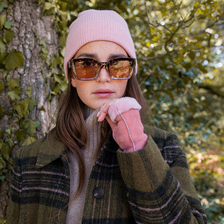 woman wearing a light pink beanie hat, sunglasses and pink suede wrist warmers
