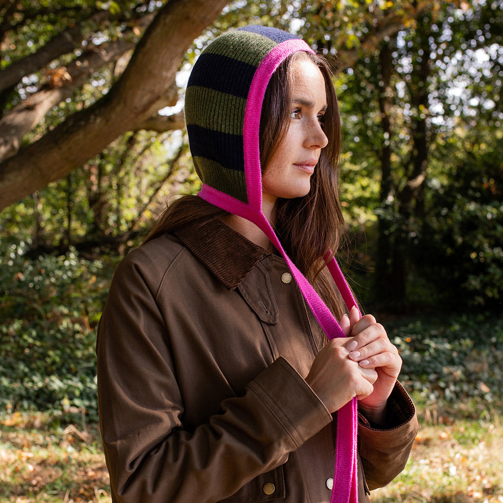 woman wearing a brown wax jacket and green & blue striped bonnet with a pink trim and ties