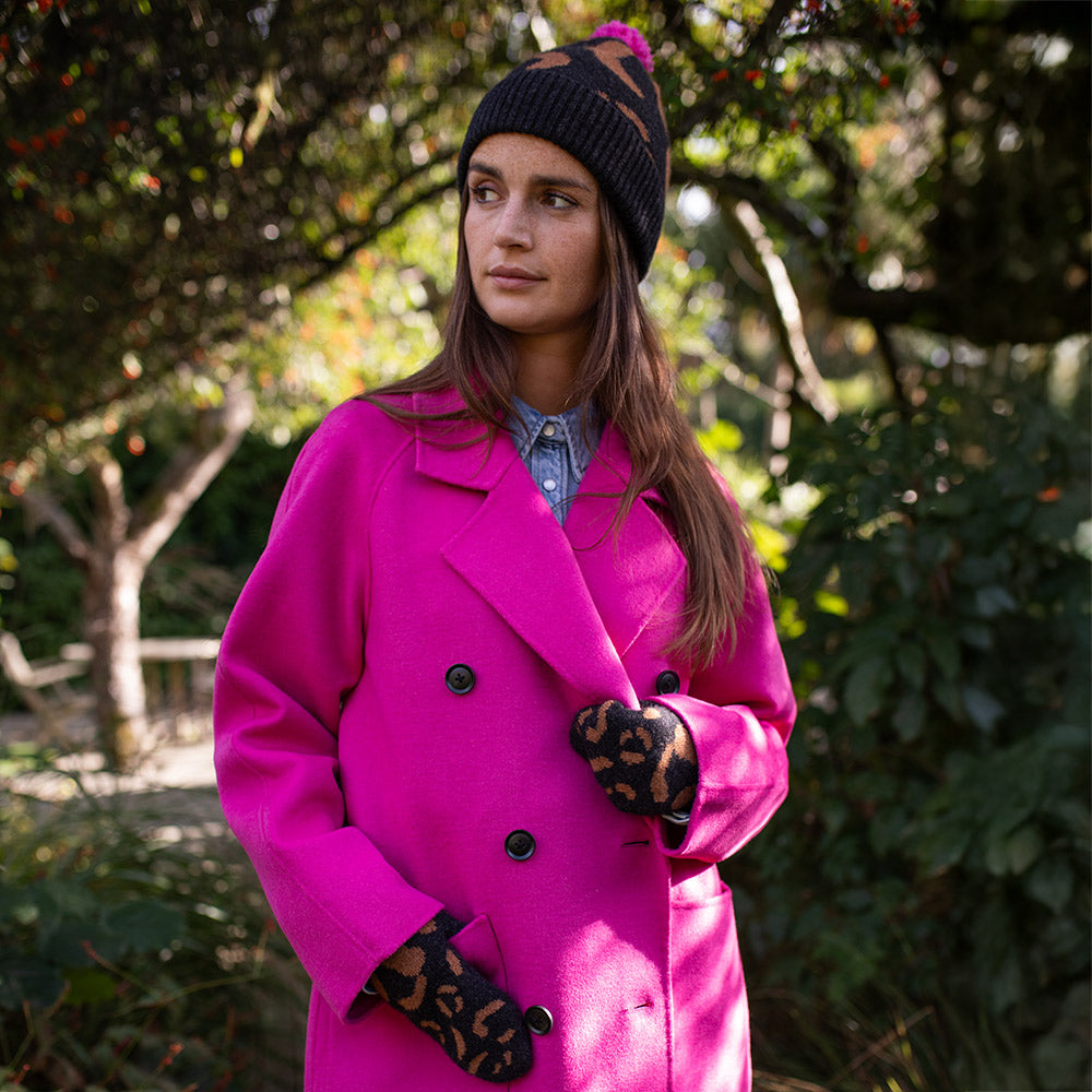 woman wearing a bright pink coat with dark grey and brown leopard print mittens and bobble hat
