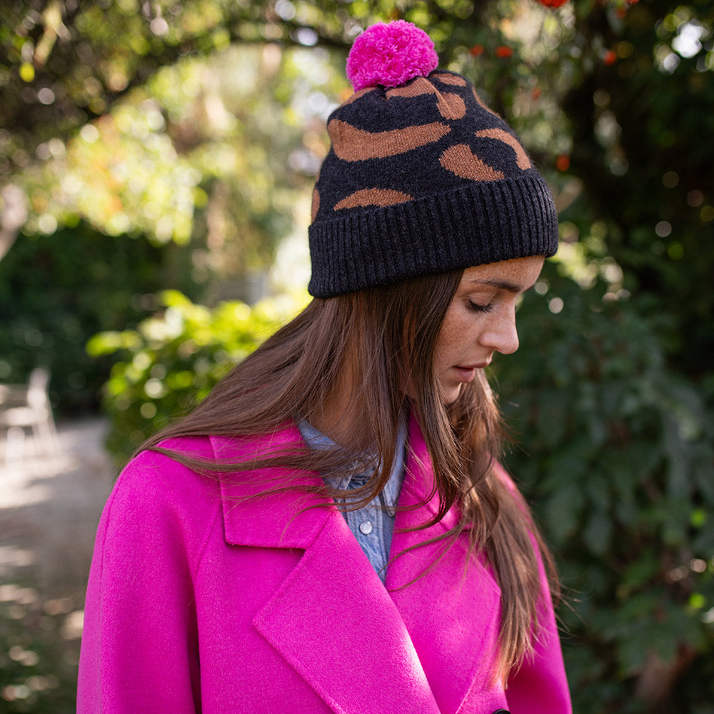 woman wearing a bright pink coat with dark grey and brown leopard print hat with a bright pink bobble