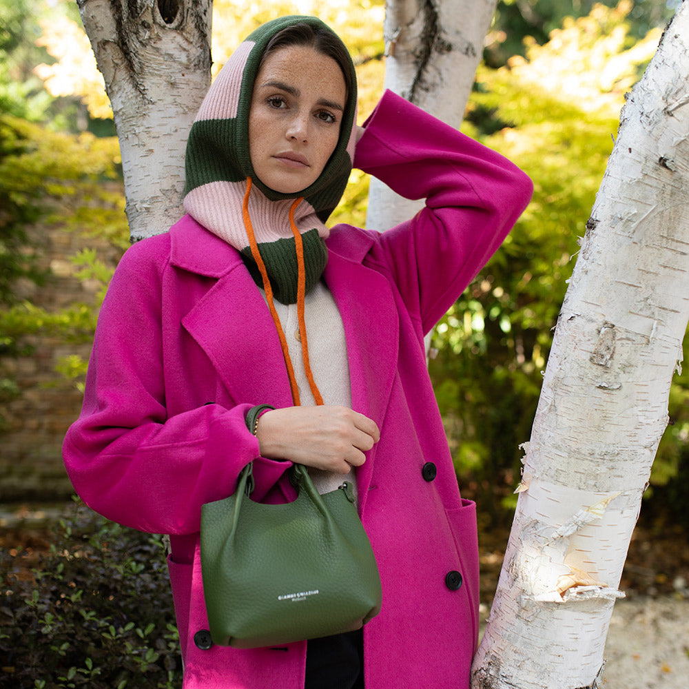 woman wearing a bright pink coat with a green and light pink striped balaclava hood with orange drawstrings