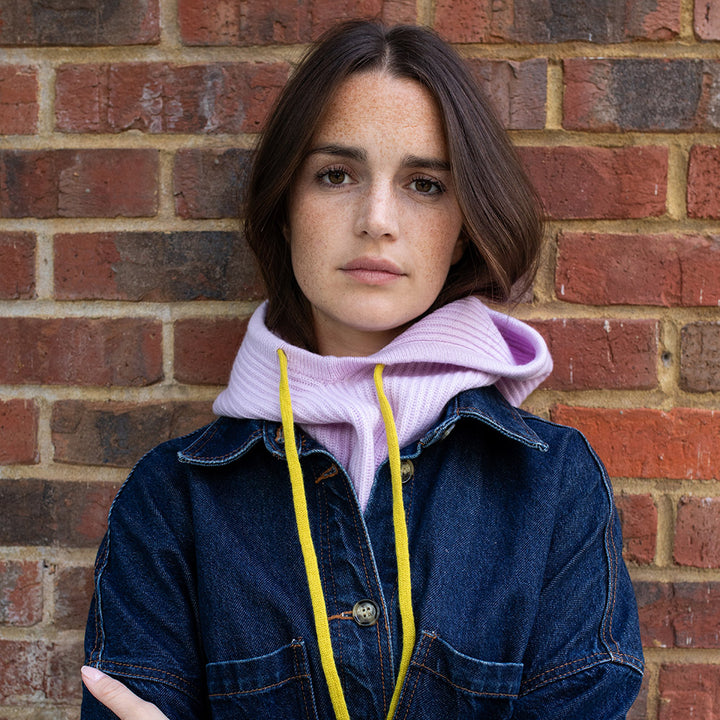 woman wearing a dark denim jacket with a lilac balaclava hood with yellow drawstrings