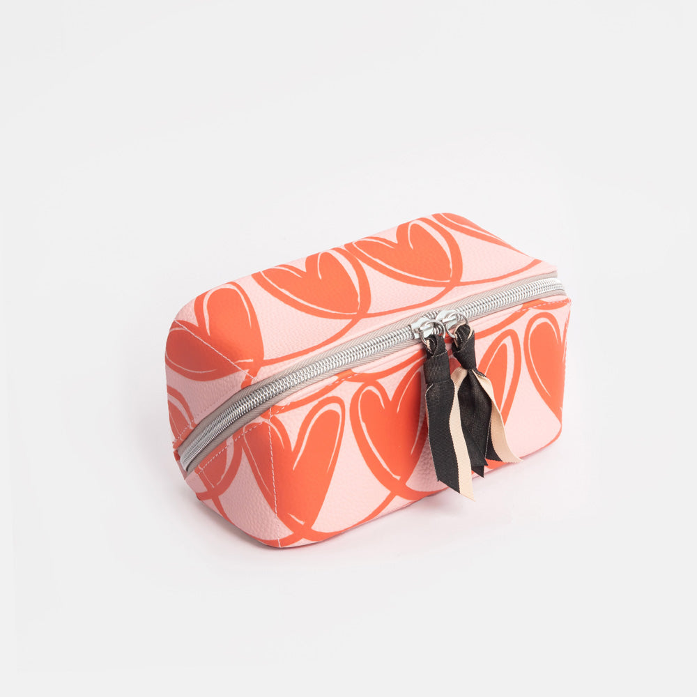 diagonal zip flat lay cosmetics bag with orange looped hearts design on pink base with black and white fabric zip pulls