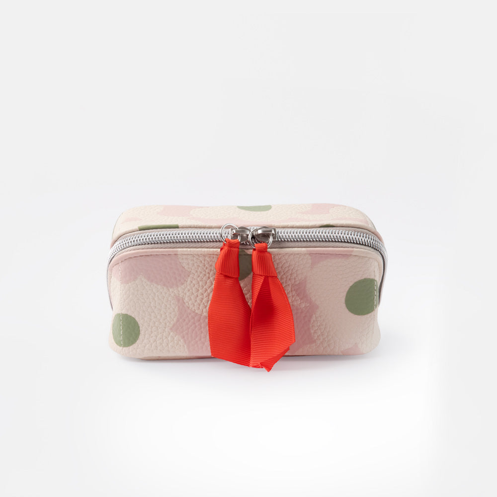 A small zippered wash bag with a light pink and white floral pattern, green polka dots, and a bright red ribbon tassel on a silver zipper, set against a plain white background.