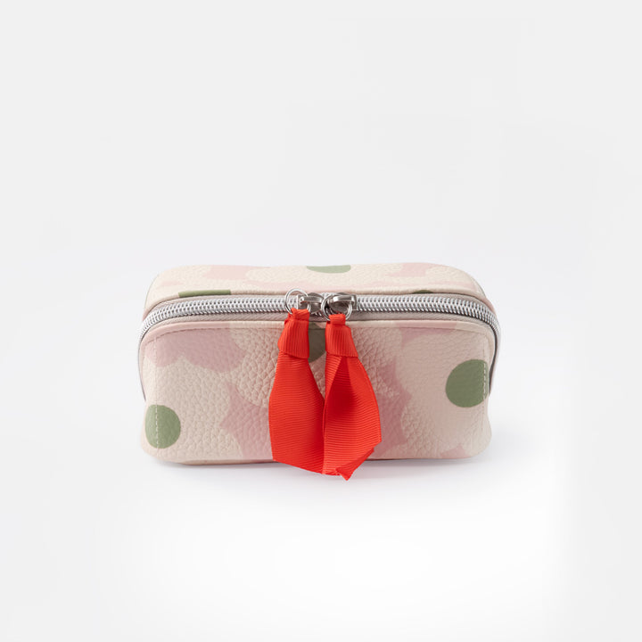 A small zippered wash bag with a light pink and white floral pattern, green polka dots, and a bright red ribbon tassel on a silver zipper, set against a plain white background.