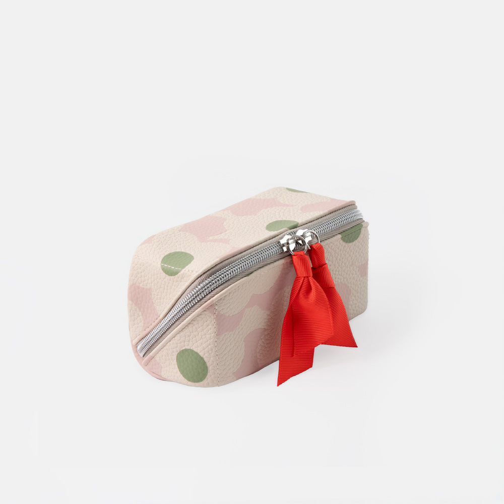 A small zippered pouch with a light pink and beige camouflage pattern, green polka dots, and a bright red fabric charm attached to the zipper.