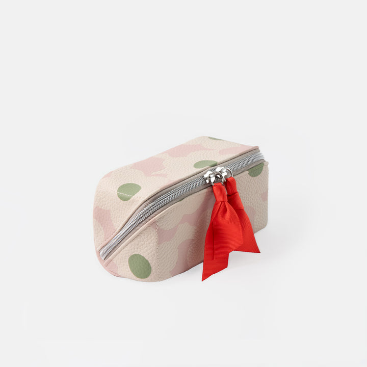 A small zippered pouch with a light pink and beige camouflage pattern, green polka dots, and a bright red fabric charm attached to the zipper.