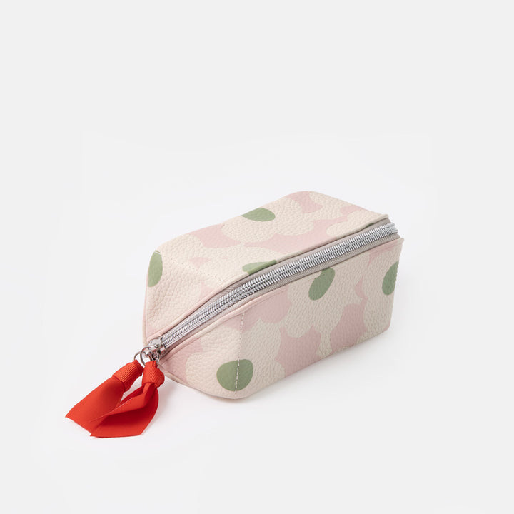 A small zippered pouch with a light pink and off-white floral pattern, green leaf accents, and a bright red fabric pull tab, shown on a plain light gray background.