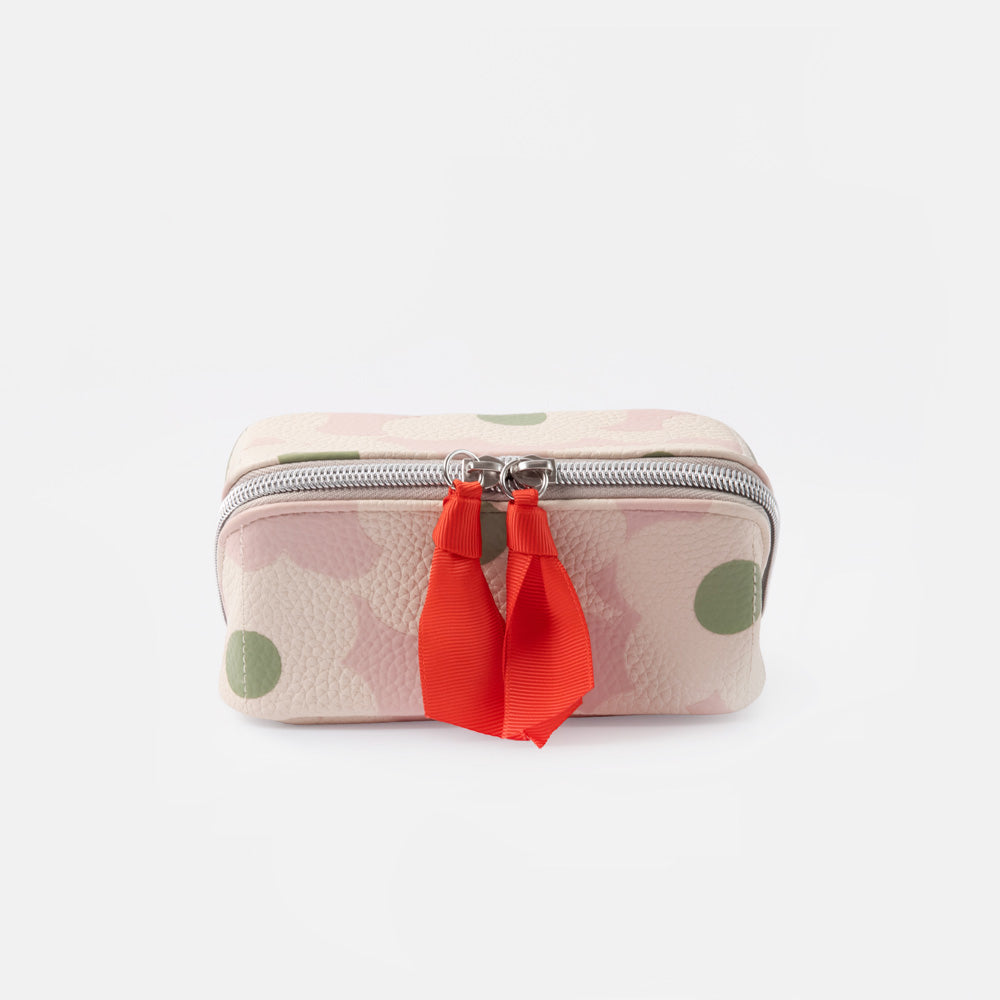 A small zippered wash bag with a light pink and white floral pattern, green polka dots, and a bright red ribbon tassel on a silver zipper, set against a plain white background.
