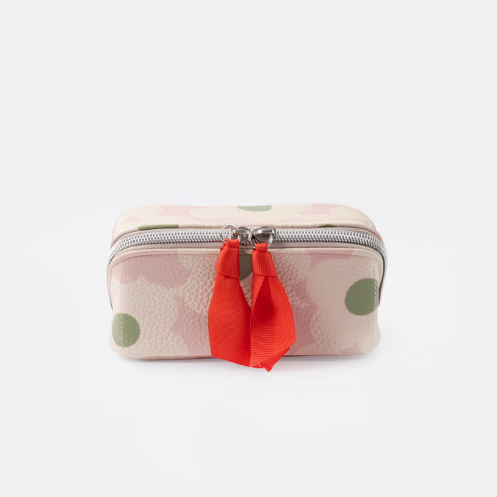A small zippered wash bag with a light pink and white floral pattern, green polka dots, and a bright red ribbon tassel on a silver zipper, set against a plain white background.
