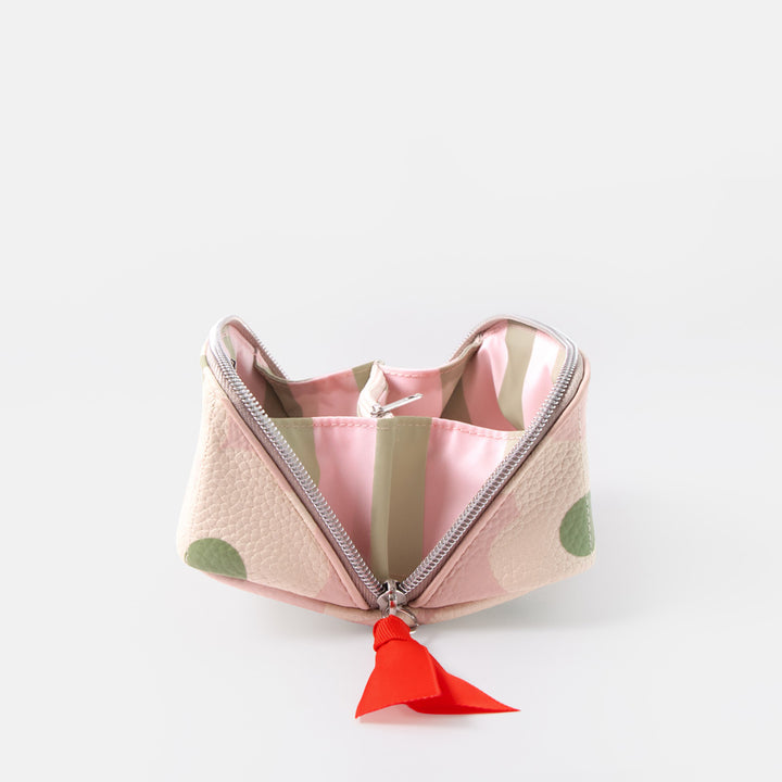 A small zippered cosmetic pouch with a textured light pink exterior, featuring green polka dots, a silver zipper, and a bright red tassel pull, shown open on a light gray background.