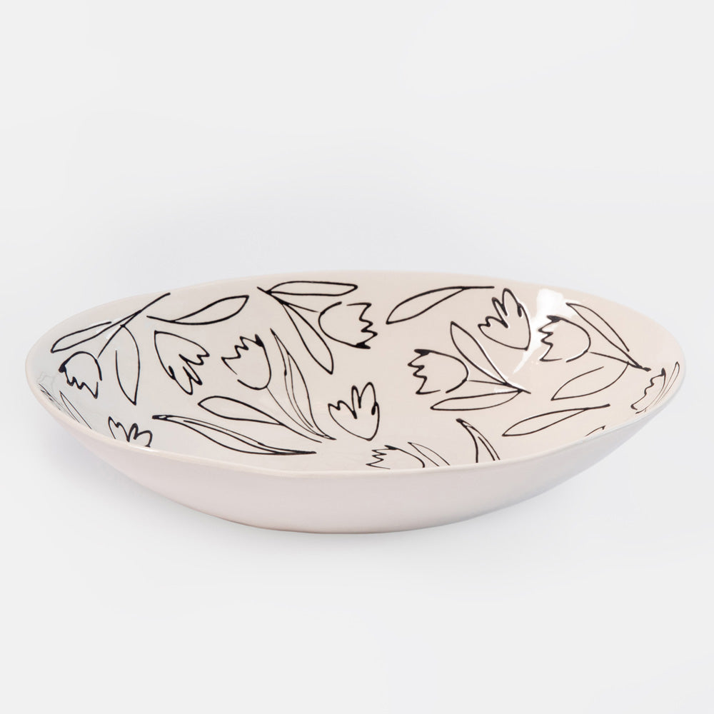 A shallow oval ceramic bowl with a light beige or cream glaze, decorated with a minimalist black line-art pattern of tulips and leaves, shown on a clean white background.