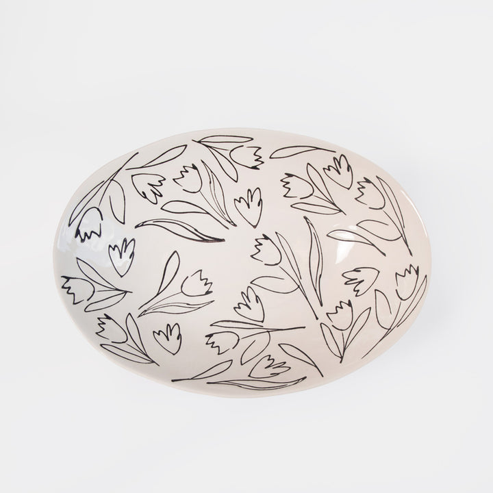 An oval ceramic dish with a glossy off-white surface decorated with a black line-art pattern of tulips, shown on a clean white background.