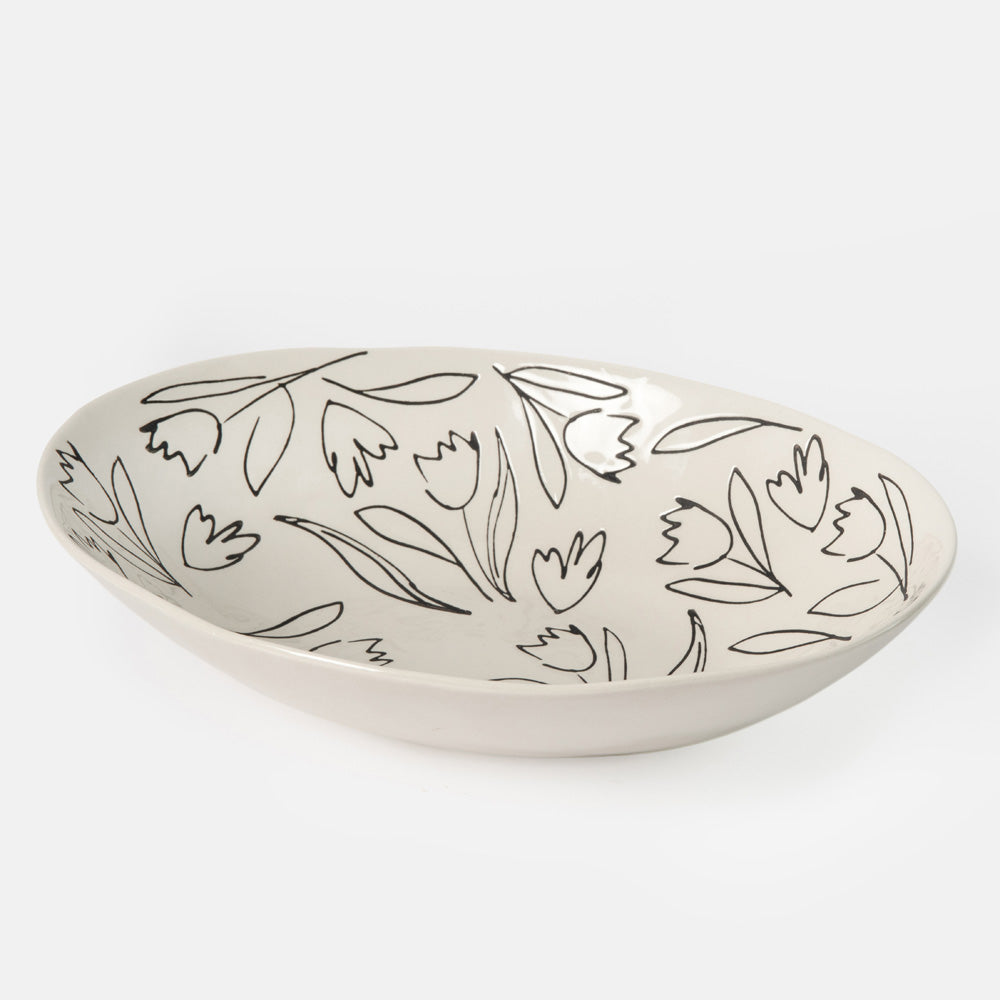 An oval ceramic bowl with a white glaze and a delicate black line-art floral pattern, photographed on a clean light gray background.